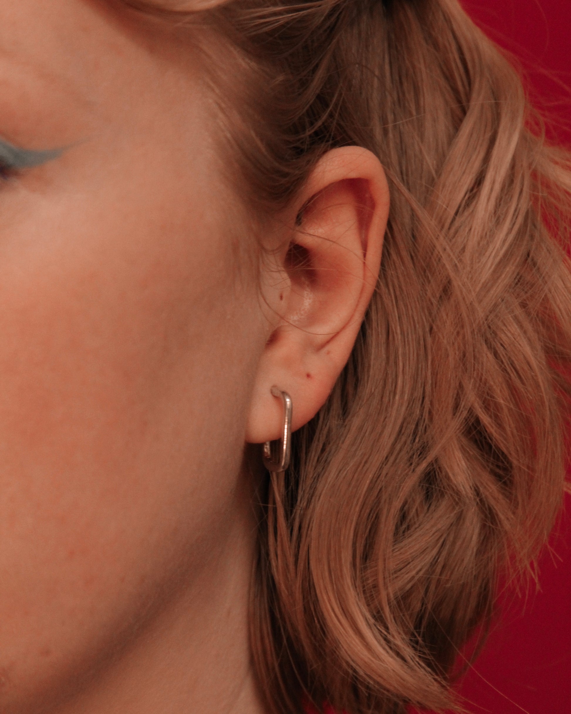 Close-up of an ear wearing a small oblong hoop earring, 925 silver. 
