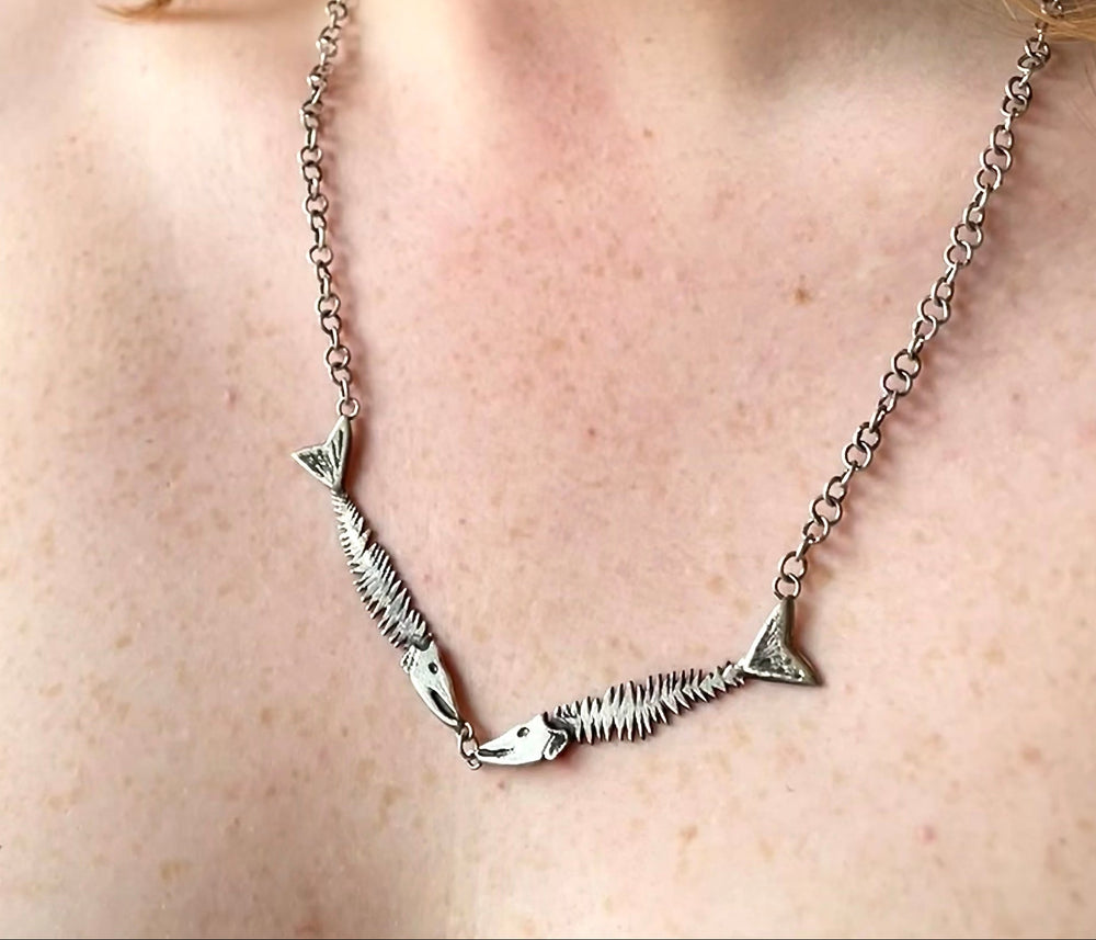 Silver necklace with 2 fish, worn by a person with a neutral background